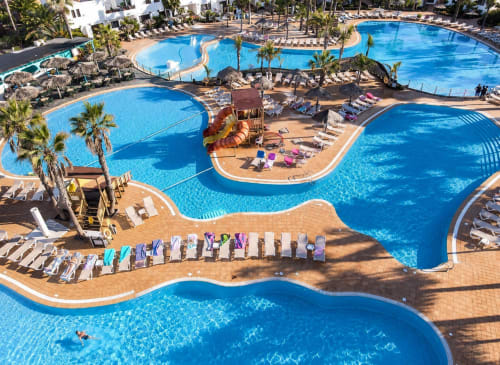 Luftaufnahme des Poolkomplexes von Sara & Gino in Fuerteventura, Corralejo, mit blauen Pools, Palmen und Liegestühlen