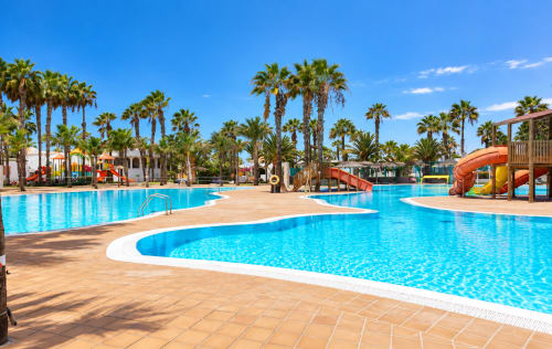 Tropischer Poolbereich im Sara & Gino Fuerteventura in Corralejo mit Palmen, Wasserrutschen und sonniger Terrasse