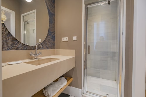 Baño moderno en Apartamentos Andimi Madrid con lavamanos flotante, espejo redondo y ducha con mamparas de cristal