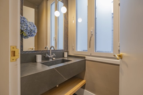 Baño moderno con tocador en piedra oscura, lámparas colgantes redondas y vistas a la ciudad en Andimi Apartamentos Madrid