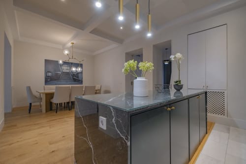 Cocina moderna de apartamento madrileño con isla de mármol, zona de comedor, lámparas colgantes y arreglos florales