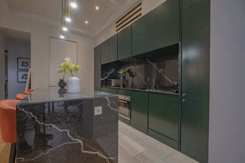 Cocina moderna con armarios verdes, isla de mármol oscuro y electrodomésticos de acero inoxidable en Andimi Apartments Madrid