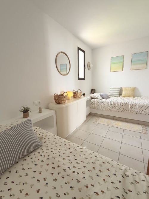 Bright beachside cottage bedroom with twin beds, woven storage baskets, coastal artwork, and modern amenities at HomyMarbella
