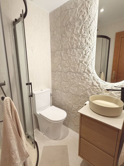 Modern bathroom with textured tile wall, white toilet, vessel sink, mirror, and black fixtures at HomyMarbella cottage in