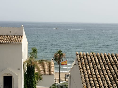 White Mediterranean townhouse with terracotta roof overlooking the sea near Marbella beach, featuring palm trees and Spanish