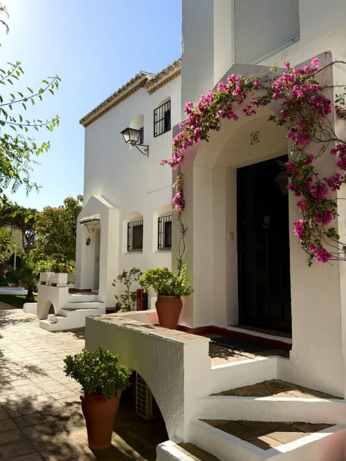 Charming white Mediterranean cottage exterior with vibrant magenta bougainvillea, terracotta planters, and black-trimmed