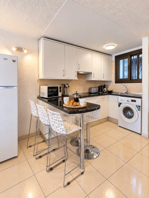 Modern kitchen with breakfast bar, white cabinets, black countertops, and appliances in Tenerife apartment