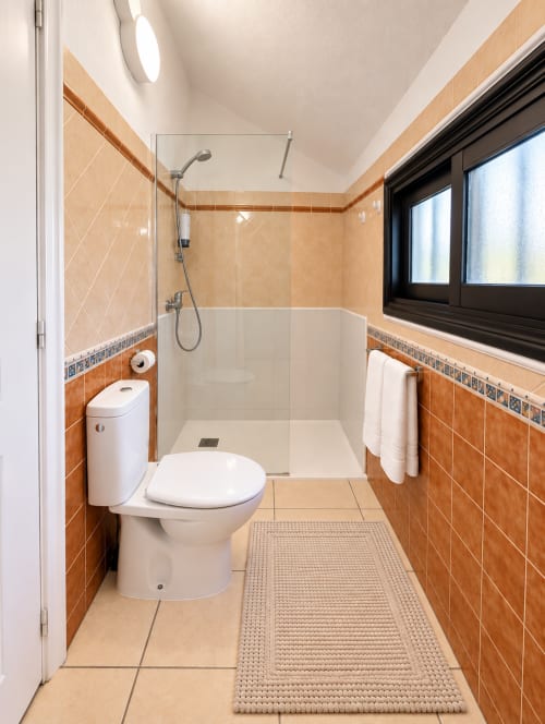 Modern bathroom at Manage Home Tenerife with orange tile walls, walk-in shower, toilet, and decorative mat in Santiago I