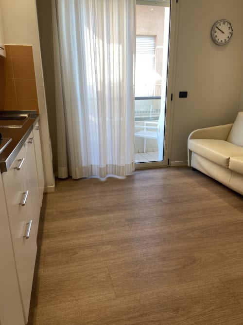 Accogliente appartamento della Residenza Aida Rimini con cucina, divano, pavimenti in legno e accesso al balcone