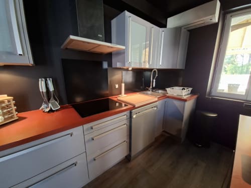 Cuisine moderne avec plan de travail orange, appareils en acier inoxydable, armoires blanches et murs sombres au Love Room Sensation