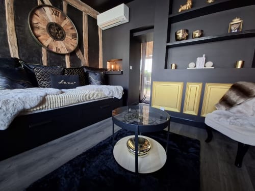 Chambre d'amour luxueuse avec sièges en velours noir, accents dorés, horloge vintage et équipements modernes au cottage-hôtel d'Esches