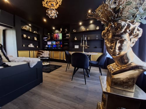 Suite de luxe aux accents dorés, murs noirs, buste, téléviseur, coin détente et mobilier élégant