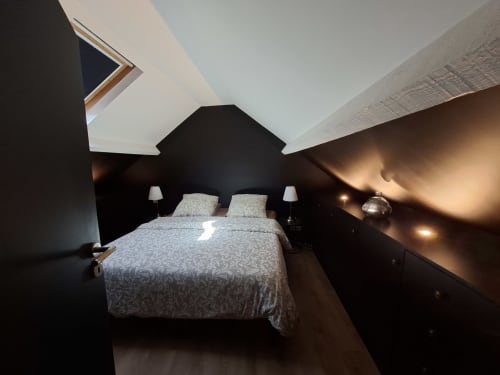 Chambre mansardée contemporaine aux murs noirs, poutres blanches au plafond, literie grise, deux lampes de chevet et éclairage ambiant - Love Room