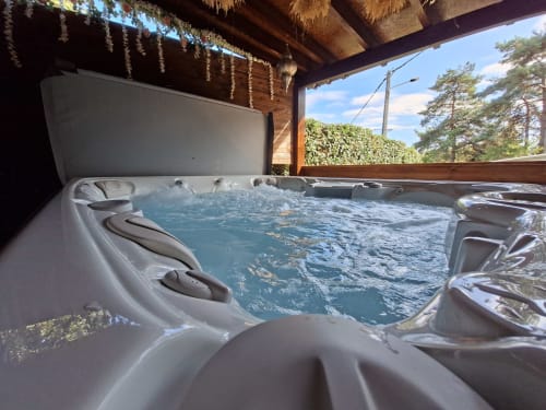 Jacuzzi bouillonnant sur terrasse en bois du gîte Love Room Sensation à Esches, France, avec vue sur le jardin et les pins