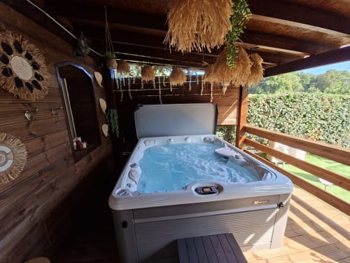 Baignoire spa extérieure sur la terrasse en bois du cottage Love Room Sensation à Esches, France, avec vue sur le jardin et pergola