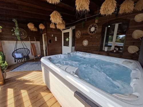 Spa Jacuzzi luxueux avec baignoire chauffée, intérieur de chalet en bois, décoration suspendue et fauteuil noir à Love Room