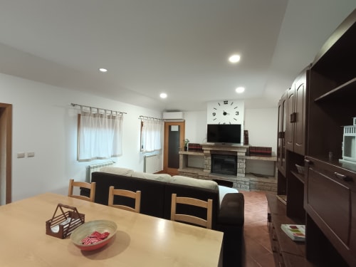Espaço de estar integrado e moderno da Quinta d'Areda com mesa de jantar, sofá preto, lareira, TV e cozinha em Fafe, Portugal