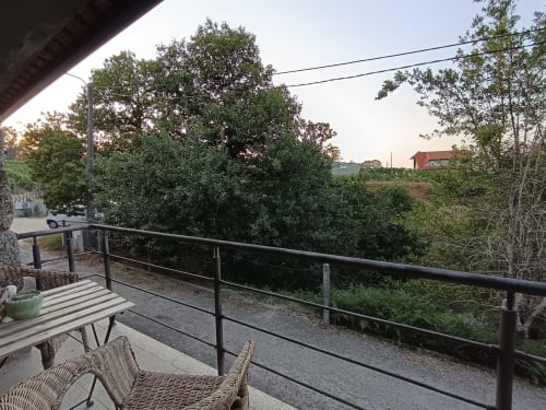 Terraço da Quinta d'Areda Wine&Pool com mobiliário em vime, varanda metálica, paisagem exuberante e casa de campo vermelha