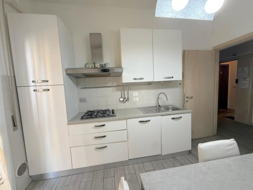 Cucina bianca moderna in appartamento fiorentino con fornello a gas, lavello, lavastoviglie e ampi spazi di ripostiglio