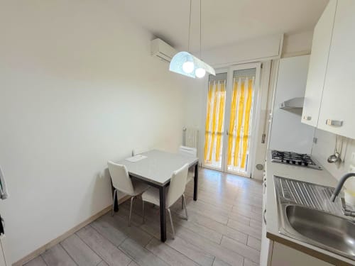 Cucina-sala da pranzo luminosa e moderna in appartamento fiorentino con mobili bianchi, tavolo da pranzo e porte-finestre gialle