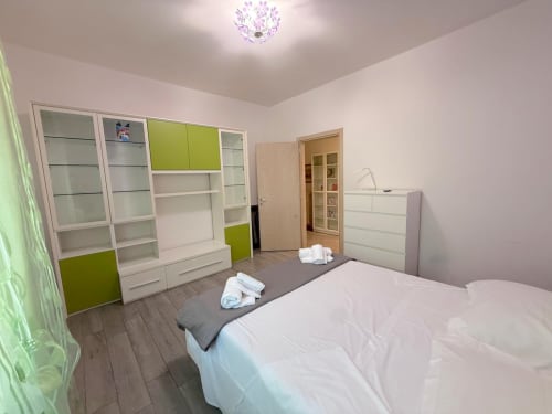 Camera da letto luminosa nell'appartamento Deledda a Firenze con letto bianco, armadio bianco e verde lime, pavimenti in legno e viola