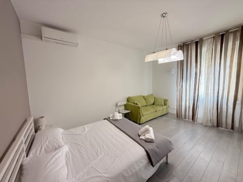 Camera da letto moderna in appartamento fiorentino con divano verde, lampada a sospensione e vista sulla città dalle porte finestre con tende