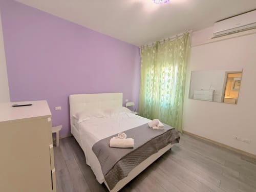 Camera luminosa a Florence Sweet Homes con parete in viola, letto bianco, tende verdi e vista sulla città a Scandicci