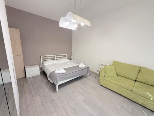 Camera da letto moderna in appartamento fiorentino con letto bianco, divano verde, lampadario a sospensione e pavimento in legno