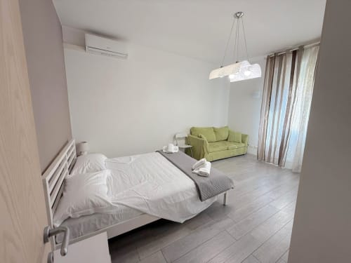 Camera da letto dell'appartamento Deledda con letto, divano verde, lampada a sospensione, aria condizionata e vista sulla città a Scandicci, Firenze