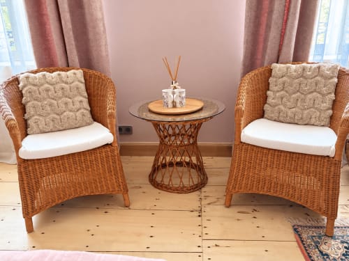 Chambre Rosalie à la Maison Crone : fauteuils en rotin douillets avec coussins beige, petite table ronde, murs roses, baies vitrées vue jardin