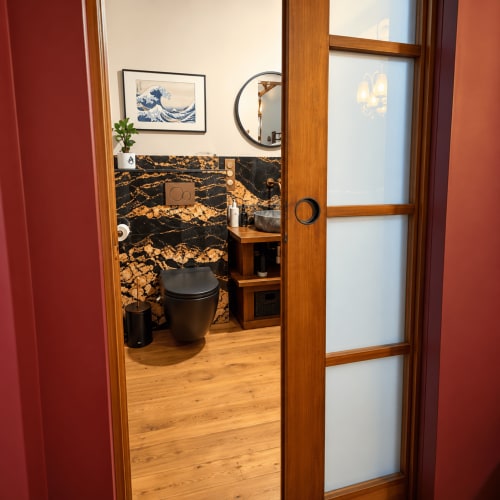 Salle de bain moderne de la Maison Crone avec murs en marbre noir et or, porte en bois et équipements minimalistes