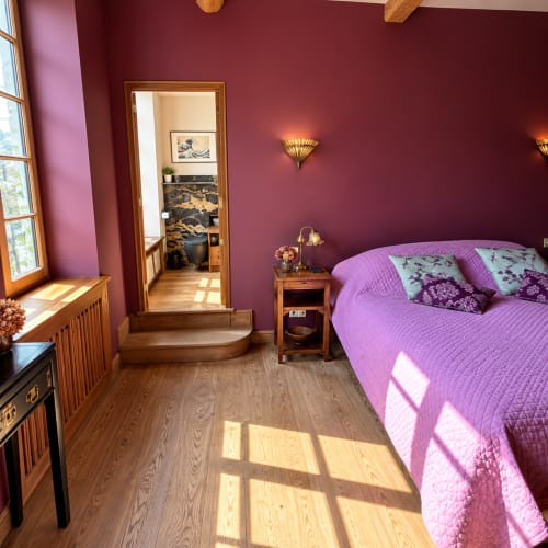 Chambre lumineuse aux murs magenta, literie violette, poutres en bois et fenêtres à la Maison Crone B&B à Castillon-en-Couserans