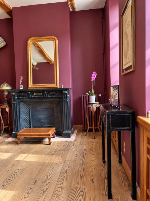 Chambre élégante à la Maison Crone avec murs bordeaux, cheminée noire, miroir doré et parquet