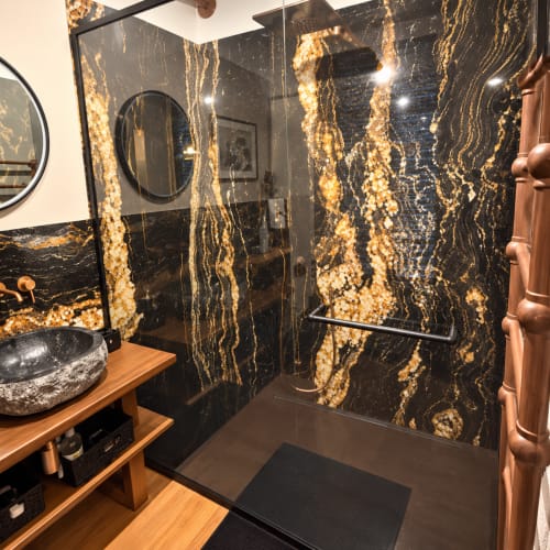 Salle de bains luxueuse avec douche en marbre noir et or, vanité en bois et accessoires en cuivre à Maison Crone