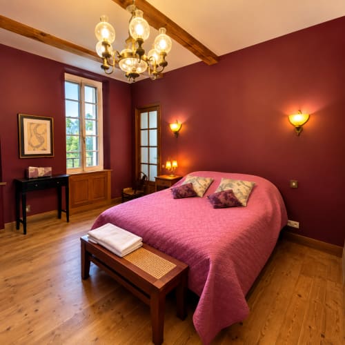 Chambre élégante à la Maison Crone B&B à Castillon-en-Couserans avec murs bordeaux, poutres apparentes et mobilier d'époque.