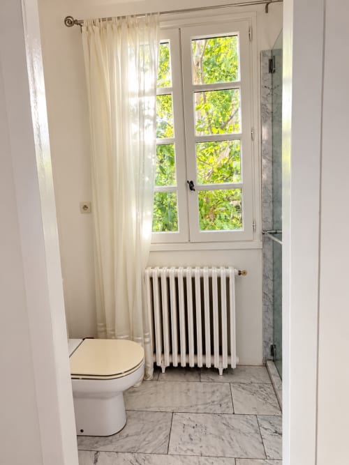 Salle de bain moderne à la Chambre Eva de Maison Crone avec carrelage marbre, radiateur vintage et vue sur le jardin par portes-fenêtres