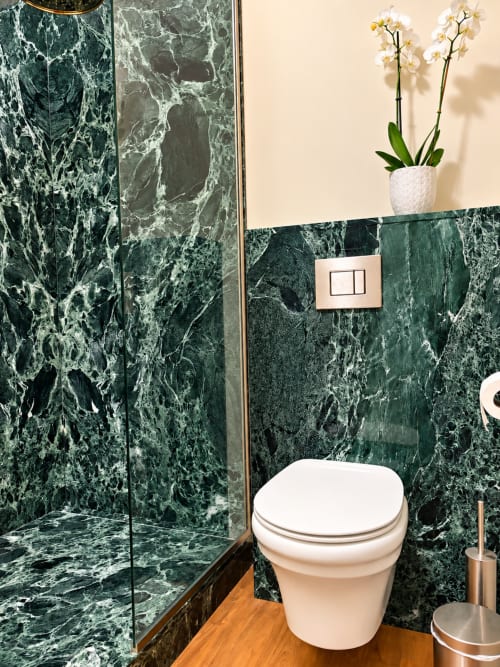 Salle de bain luxueuse à la Maison Crone avec murs en marbre vert, toilettes blanches, plante d'orchidée et accessoires en bronze