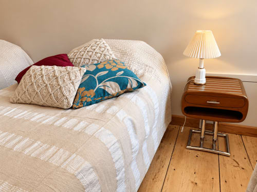 Chambre accueillante à la Maison Crone avec literie blanche texturée, coussins décoratifs, table de nuit en bois et lampe