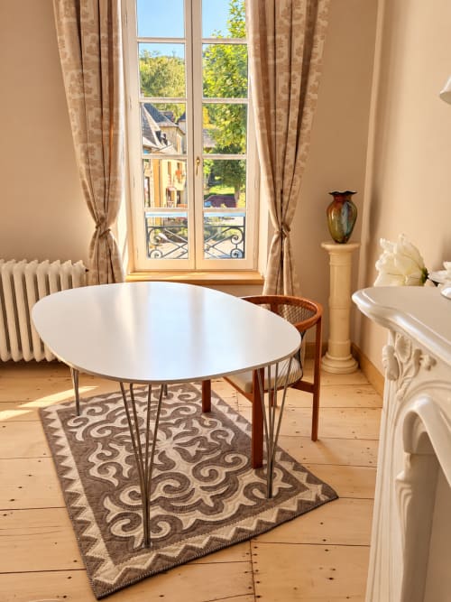 Salle à manger de la Maison Crone avec table ronde blanche, chaises en bois, tapis à motifs et fenêtres donnant sur Castillon-en-Couserans