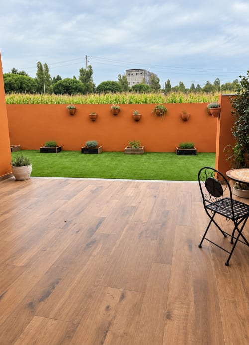 Terraço com deck de madeira, parede laranja e jardim exuberante na House Park B&B em Esposende, Portugal