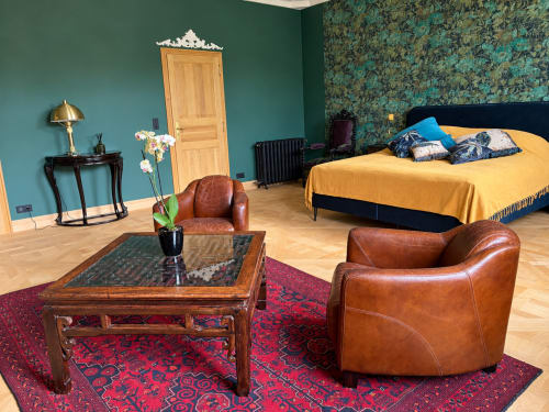 Chambre Émeraude à la Maison Crone B&B avec murs bleu-vert, fauteuils en cuir, lit en bois avec parure jaune et papier peint fleuri