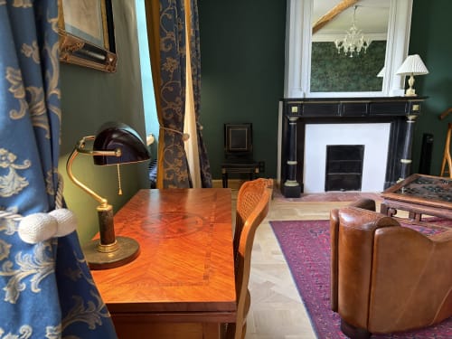 Chambre élégante émeraude à la Maison Crone avec cheminée, bureau en bois, sièges en cuir et vue sur le jardin