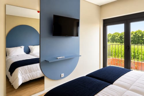 Quarto moderno da House Park com camas de solteiro, parede azul destaque, TV e varanda com vista para paisagem montanhosa verde