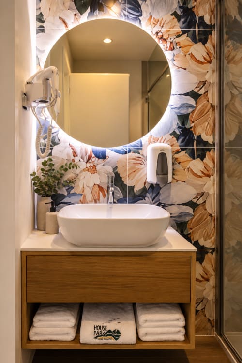 Banheiro moderno do hotel House Park em Esposende com lavatório branco, espelho redondo iluminado e papel de parede floral
