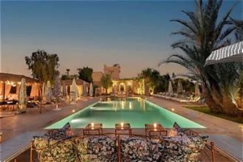La piscine rectangulaire illuminée du Riad Casa Angelo au crépuscule avec transats, palmiers et architecture marocaine traditionnelle