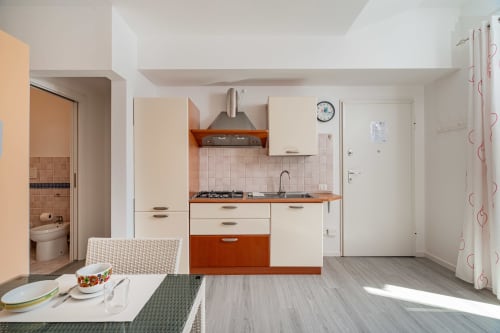 Modern kitchenette with dining area at Short Let's Olbia apartment, featuring cream and orange cabinetry, gas stove, and