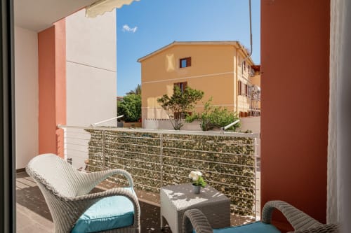 Sunny balcony at Short Let's Olbia with wicker furniture, green privacy screen, and yellow building views in Olbia, Italy
