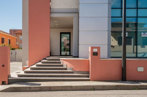 Modern entrance of Short Let's Olbia hotel with red and white facade, stone steps, and glass doors in Olbia, Italy