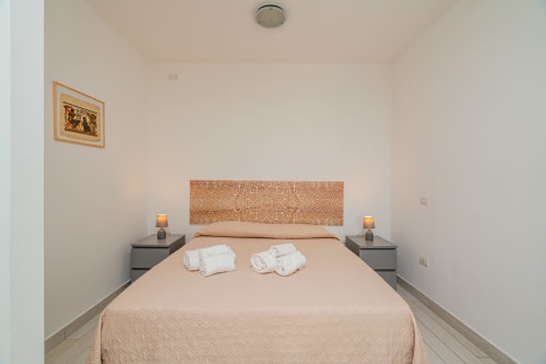 Cozy bedroom at Short Let's Olbia with peach bedding, patterned headboard, twin nightstands with lamps, and framed artwork.