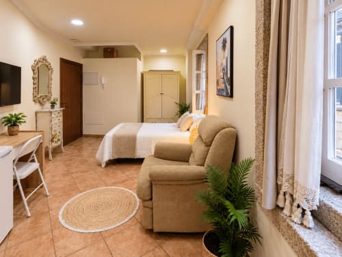 Estudio Amodiño en Baiona con sillón beis, cama, escritorio, TV y vistas a la ciudad
